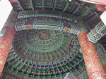 Ceiling in the Imperial Vault of Heaven.  The Imperial Vault of Heaven is one of the three key buildings in the Park - the other two are The Hall of Prayer for Good Harvests and the Circular Mound Altar.  These buildings are unique both for the unusual geometric layout and because they supposedly represent the pinnacle of traditional Chinese architecture.  The buildings are linked by a 1000 foot, raised passage, running north/south. On the north end is the Hall of Prayer for Good Harvests and to the south, the Imperial Vault of Heaven the Circular Mound Altar (Huan-ch'iu t'an).  Seen from the air, the wall of the enclosure to the south is square, while the one on the north side is semicircular. This pattern symbolizes the traditional Chinese belief that heaven is round and earth square.  The Imperial Vault of Heaven, first erected in 1530 and rebuilt in 1752, is some 64 feet high and about 50 feet in diameter. The circular building has no crossbeam, and the dome is supported by complicated span work. Its decorative paintings still retain their fresh original colors.
