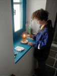 Maggie lighting the oil lamp with a candle.  This picture shows the oil lamp paraphenalia one finds in nearly every church, including some paper on which to wipe one's fingers